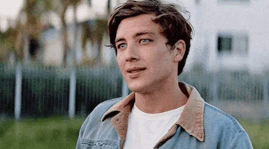 a young man wearing a denim jacket and a white shirt is smiling .