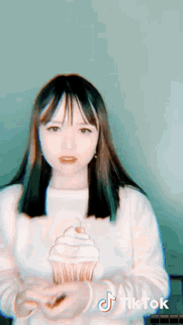 a girl wearing a white sweater with a cupcake on it has a tiktok logo on her shirt