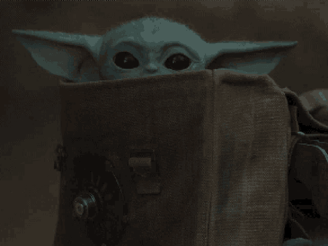 a baby yoda is hiding behind a brown cloth