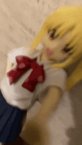 a doll with blonde hair and a red bow is laying on a bed .
