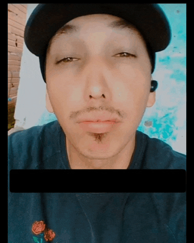 a man wearing a hat and ear buds is taking a selfie