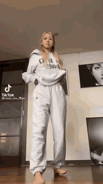 a woman in a white hoodie and white sweatpants is standing in a room .