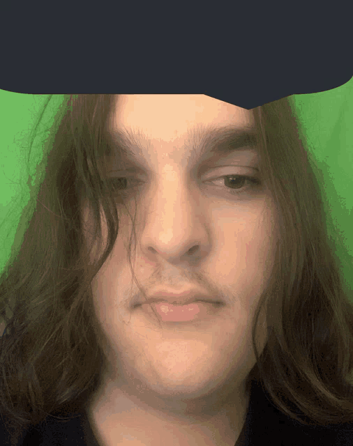 a man with long hair and a mustache looks at the camera with a green background
