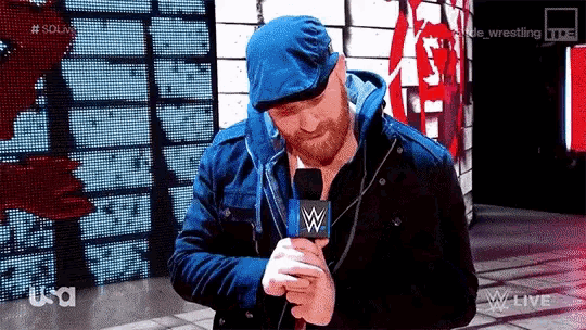 a man with a beard is holding a microphone and wearing a blue hat .