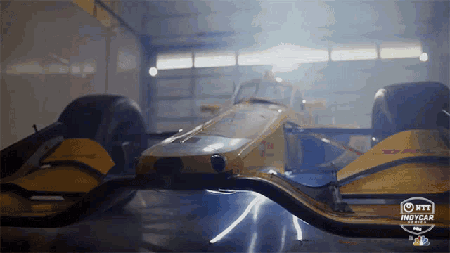 a yellow race car is sitting in a garage with the indycar series logo