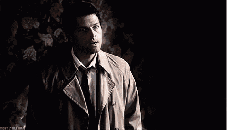 a man in a trench coat and tie is standing in the dark looking up .