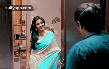 a woman in a blue saree is standing in front of a mirror .