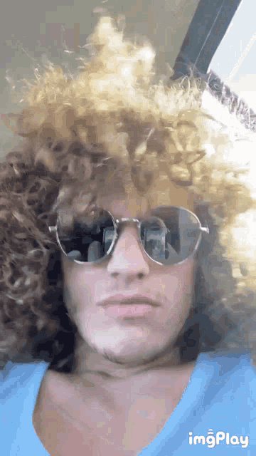 a man with curly hair wearing sunglasses and a blue shirt with imgplay written on the bottom