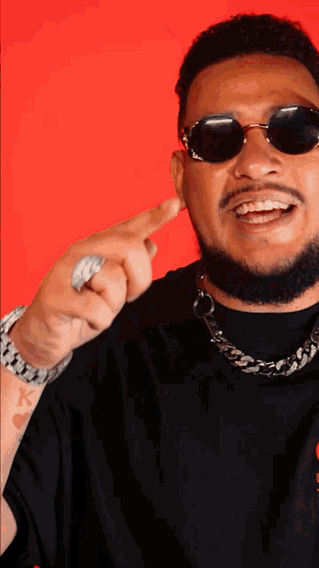 a man wearing sunglasses and a ring has a tattoo on his wrist that says k