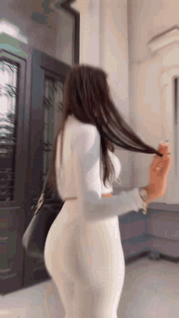 a woman in a white dress is standing in front of a door holding her hair .