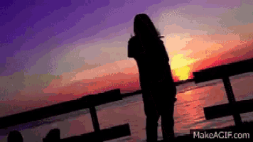 a silhouette of a person standing on a pier at sunset