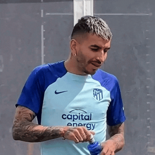 a man is drinking water from a bottle while wearing a blue shirt that says capital energy .