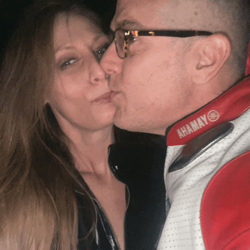 a man kisses a woman on the cheek while wearing a red and white yamaha jacket