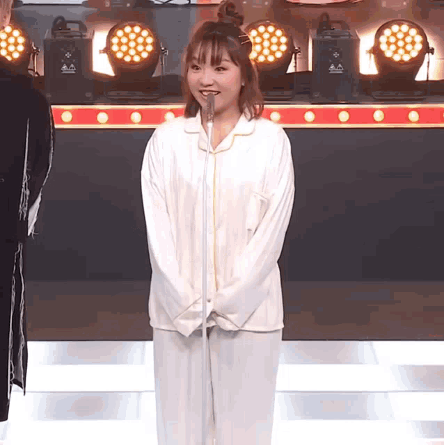 a woman in pajamas stands in front of a microphone with a sign that says ' aa ' on it