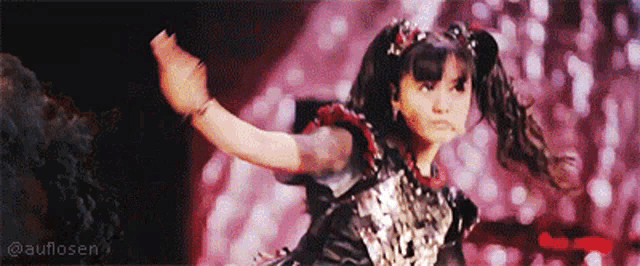 a young girl is dancing on a stage with her arms outstretched in front of a pink background .