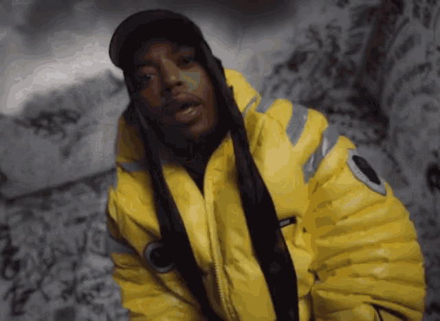 a man wearing a yellow jacket and a black hat with the word supreme on it
