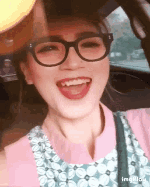 a woman wearing glasses and a pink shirt smiles in a car
