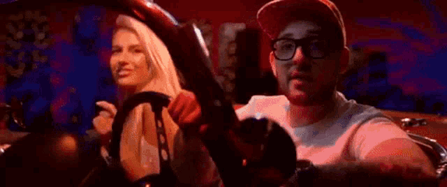 a man wearing glasses is driving a car with a woman in the background .
