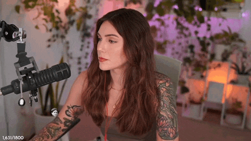 a woman with tattoos on her arms is sitting in front of a microphone in a room .