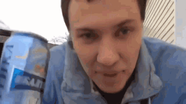 a man in a blue jacket is drinking from a can of soda .
