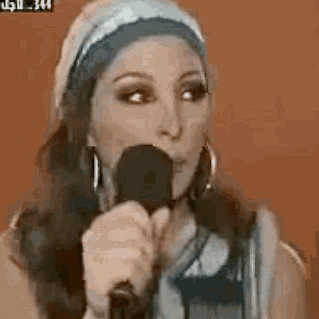 a woman is singing into a microphone while wearing a headband and hoop earrings .