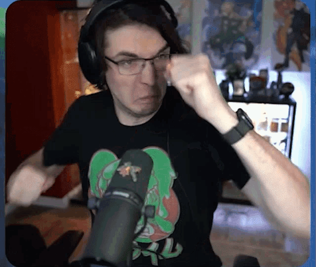 a man wearing glasses and headphones stands in front of a microphone with his fist raised