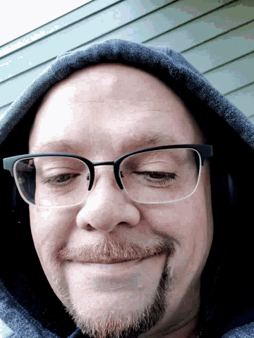 a man with glasses and a beard is wearing a hooded jacket