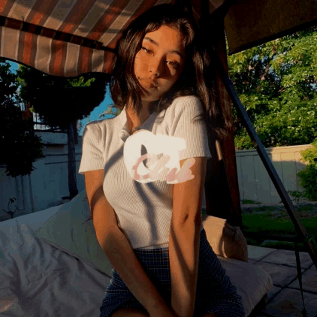 a woman in a white shirt and plaid skirt is sitting on a bench