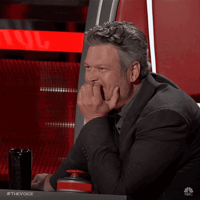 a man sitting at a table with his hand on his chin and a nbc logo on the bottom right