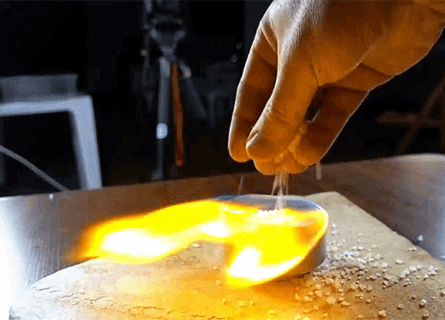 a person 's hand is pouring salt into a small container that is on fire