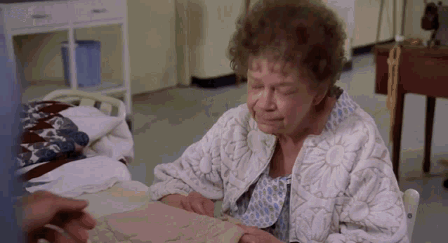 an elderly woman is sitting in a hospital bed looking at a piece of paper .