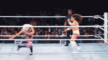 two women wrestling in a ring with a referee watching