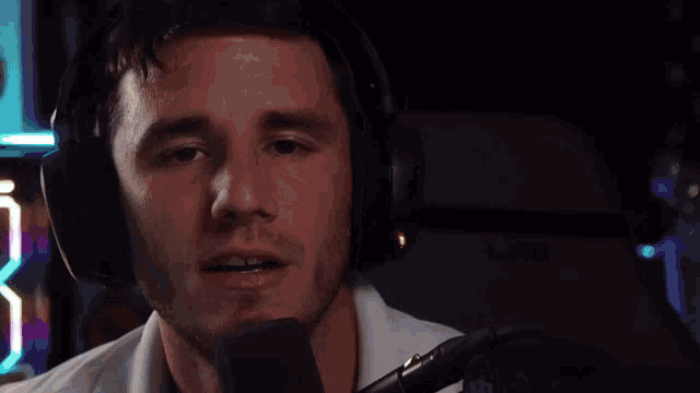 a man wearing headphones is talking into a microphone with the words what are you doing behind him