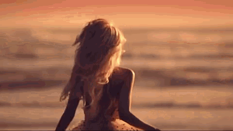 a woman is sitting on the beach at sunset looking at the ocean .