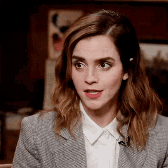 a woman in a suit and white shirt is making a funny face while talking on a microphone .