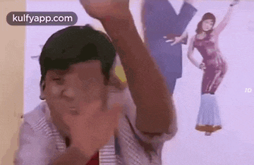 a man is making a funny face in front of a picture of a woman dancing .