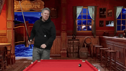a man stands in front of a pool table with a saloon sign behind him