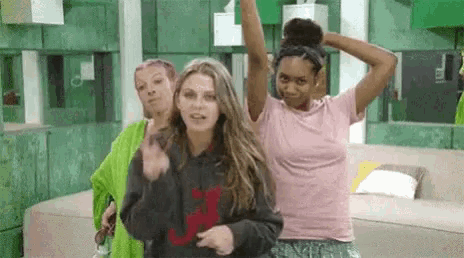 three women are dancing together in a room with a green wall .