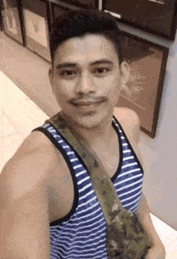 a man wearing a striped tank top is standing in front of a wall of pictures