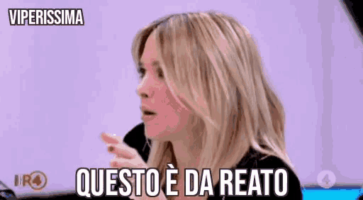 a woman with blonde hair is sitting in front of a sign that says viperissima questo e da reato .