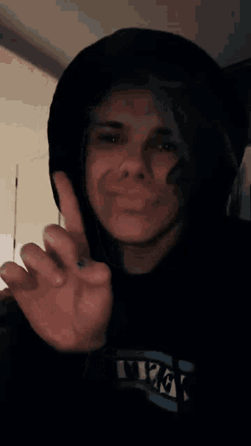 a person wearing a black hoodie with the letter k on it making a peace sign