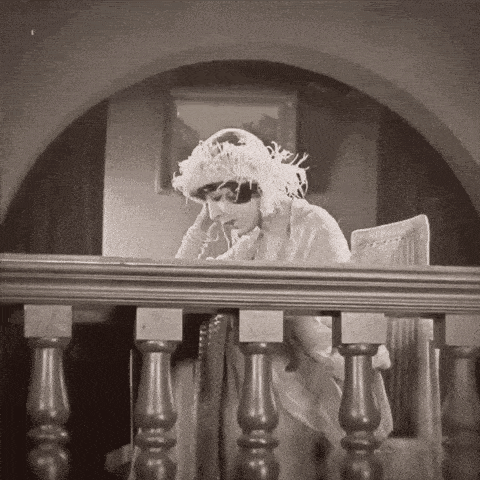 a woman in a feathered hat sits on a balcony looking down