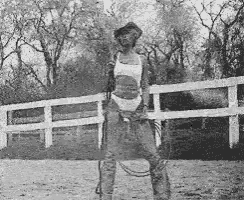 a woman is standing in front of a white fence holding a lasso .