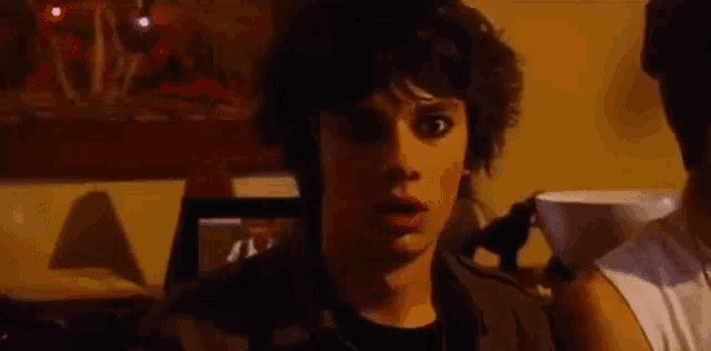 a young man with a surprised look on his face is standing in a dark room .