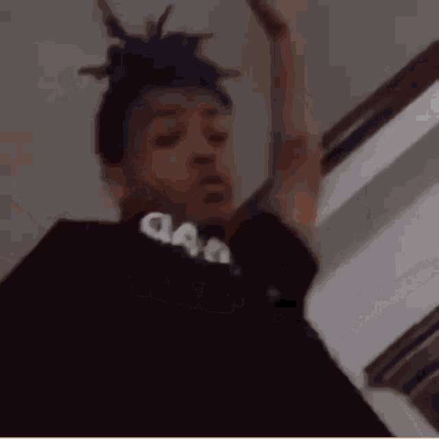 a man with blue hair and dreadlocks is standing in a room with his arms in the air .