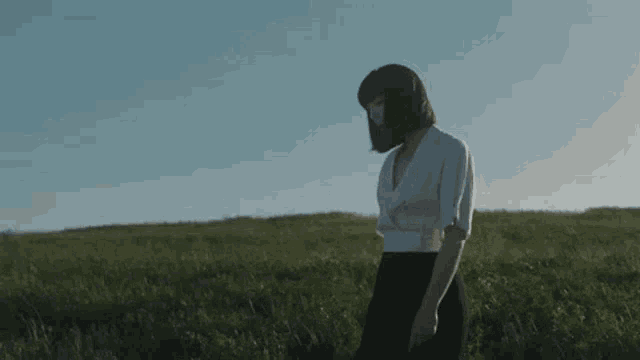 a woman is walking through a grassy field with her head down .