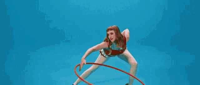 a woman is holding a red hula hoop in her hands while dancing on a blue background .