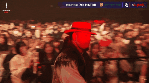a man in a red hat stands in front of a crowd with the words round 8 7th match on the screen behind him