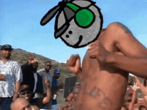 a man without a shirt is dancing in front of a crowd of people with a cartoon character on his head .