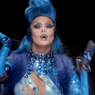 a woman with blue hair and blue jewelry is wearing a blue octopus costume and making a funny face .
